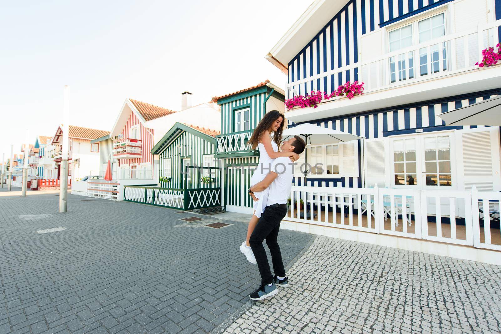 Young couple in white clothes walks around street in Aveiro, Portugal near colourful and peaceful houses. Lifestyle. Having fun, laughs, smiles.