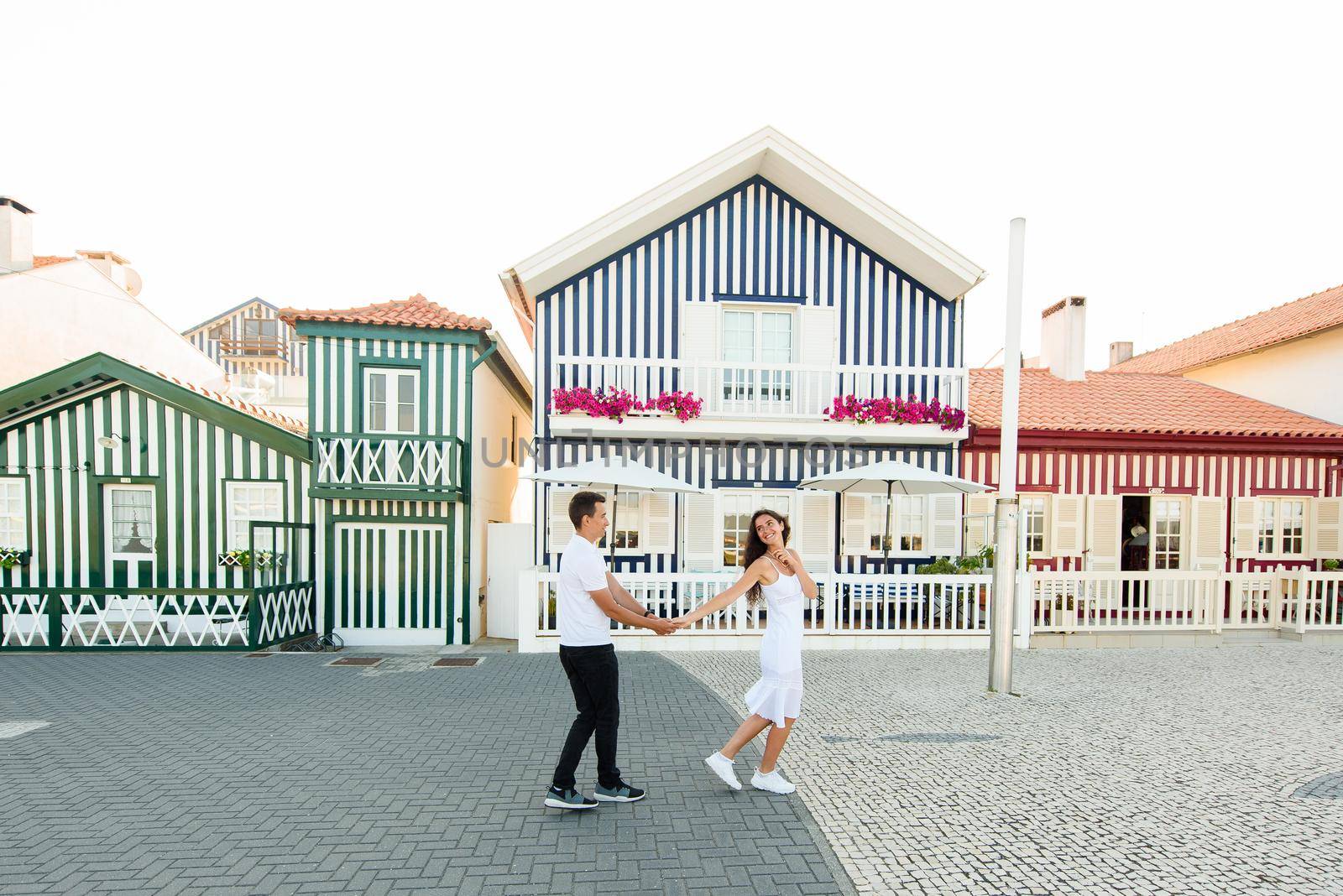 Young couple in white clothes walks around street in Aveiro, Portugal near colourful and peaceful houses. Lifestyle. Having fun, laughs, smiles
