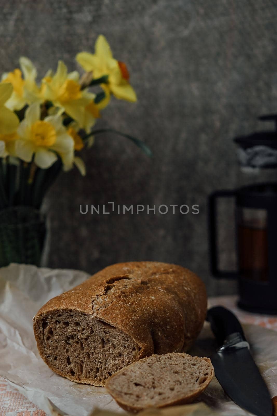 A round loaf of a crusty bread, on a rustic wooden table with scattered flour. Next to it lies a bread knife