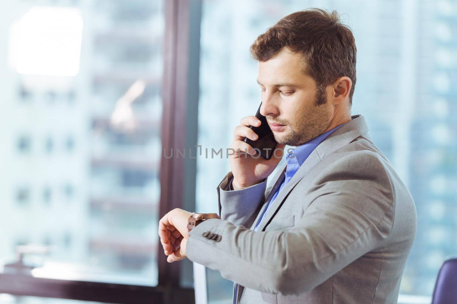 Business man looking at his watch while calling to partner in office, business time concept.