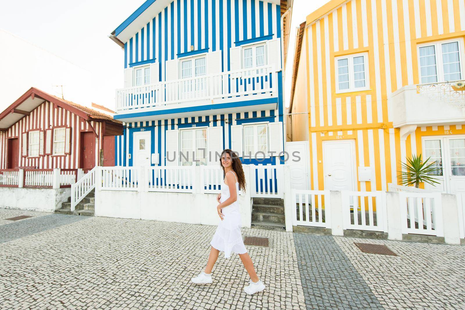 Young girl in white dress walks around street in Aveiro, Portugal near colourful and peaceful houses. Lifestyle.