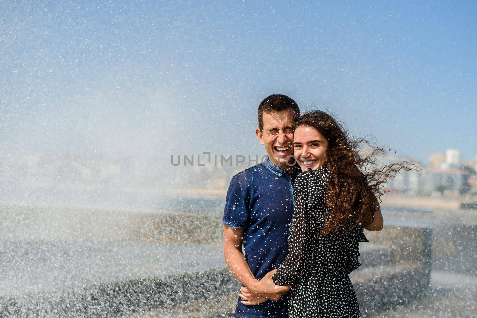 Splashing a wave of the ocean on two people in love. Lifestyle of couple. Having fun and laughs. Porto, Portugal, near Atlantic ocean by Rabizo