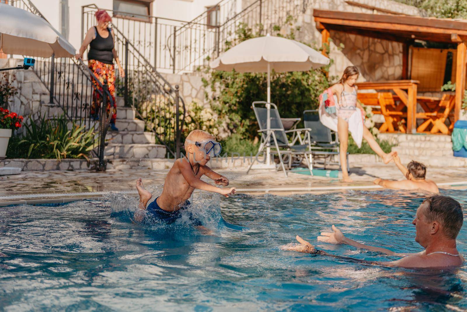 Excited boy in googles jumping in water from shoulders of his father standing in swimming pool