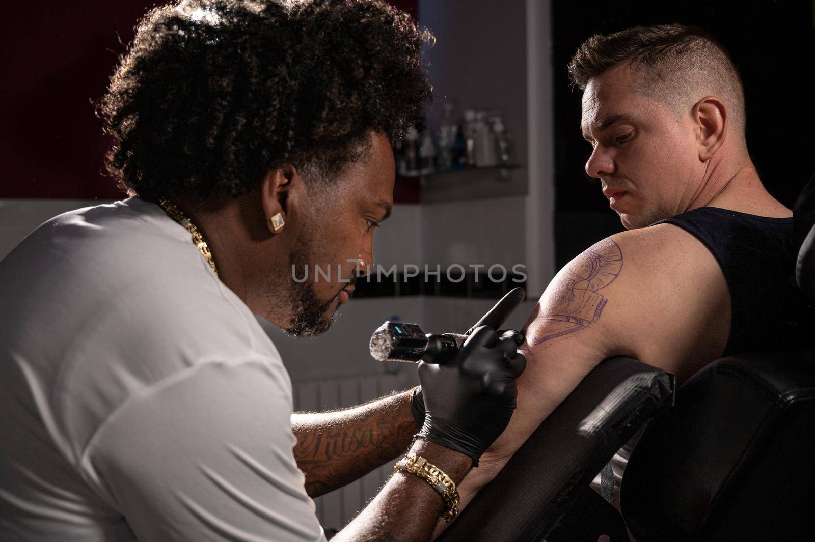 Professional African American tattoo artist makes a tattoo on client arm. High quality photography.