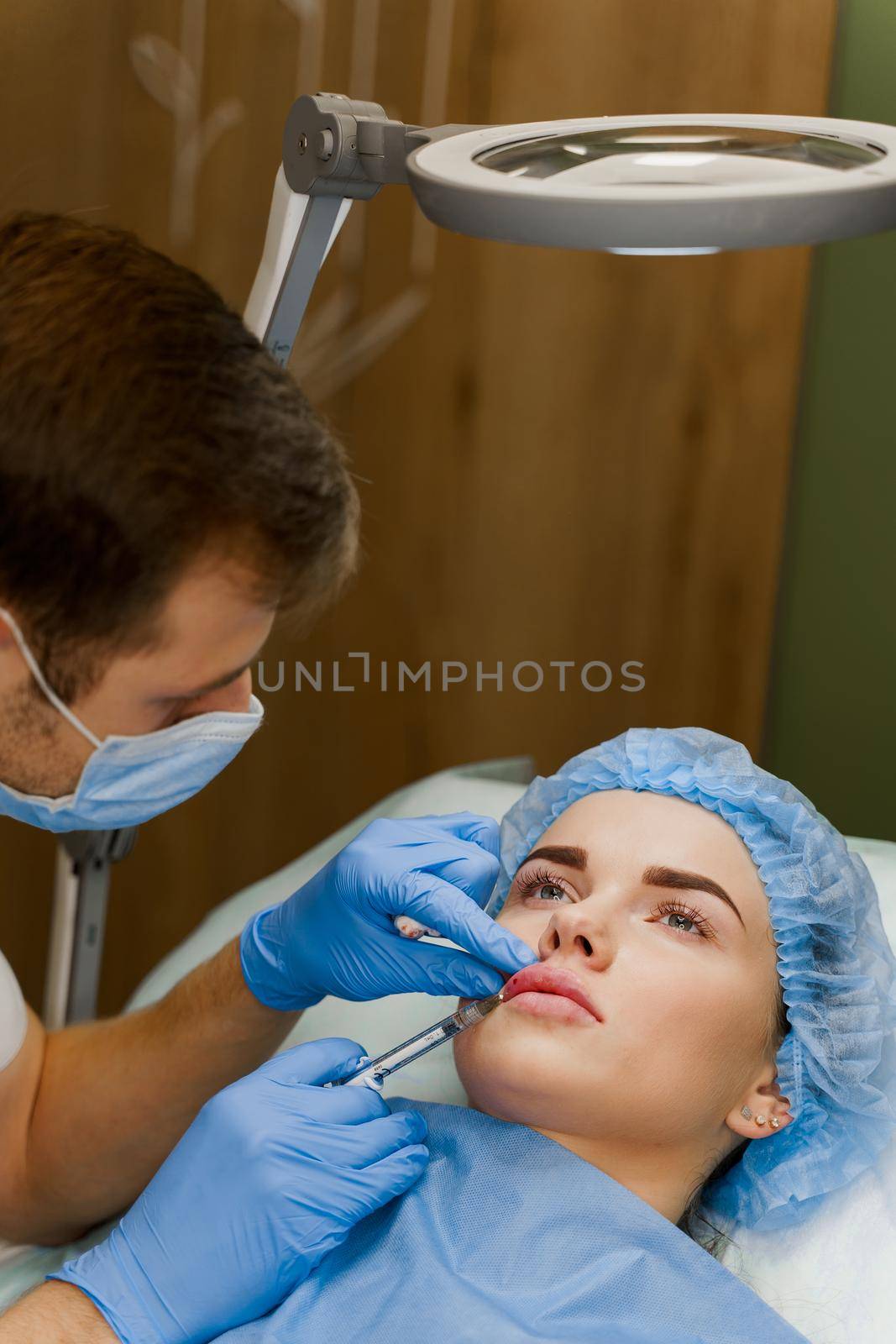 Lips augmentation injections for attractive girl. Plastic surgeon does injection in lip in medical clinic. Cosmetic rejuvenating facial treatment.