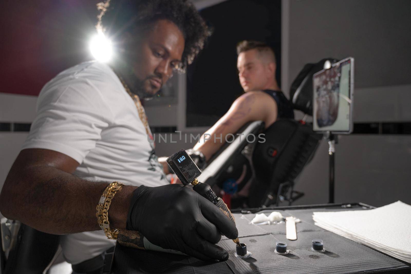 Professional African American tattoo artist makes a tattoo on client arm by HERRAEZ
