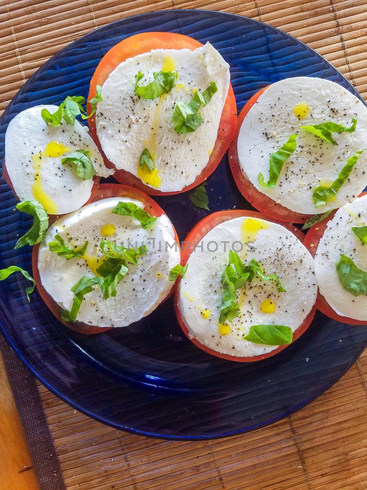 Keto style fresh Italian caprese salad. Mozzarella slices served on slices of beefsteak tomatoes, topped with fresh chopped basil, olive oil, salt and black pepper.