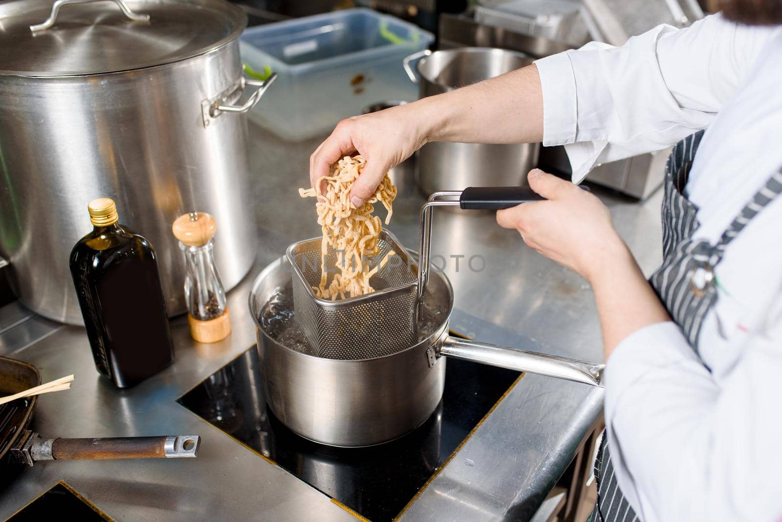 Noodles are put in the pan on kitchen. Chef cooks spaghetti noodles for ramen soup. Cooking ramen soup with meat, mushrooms, radish, eggs.