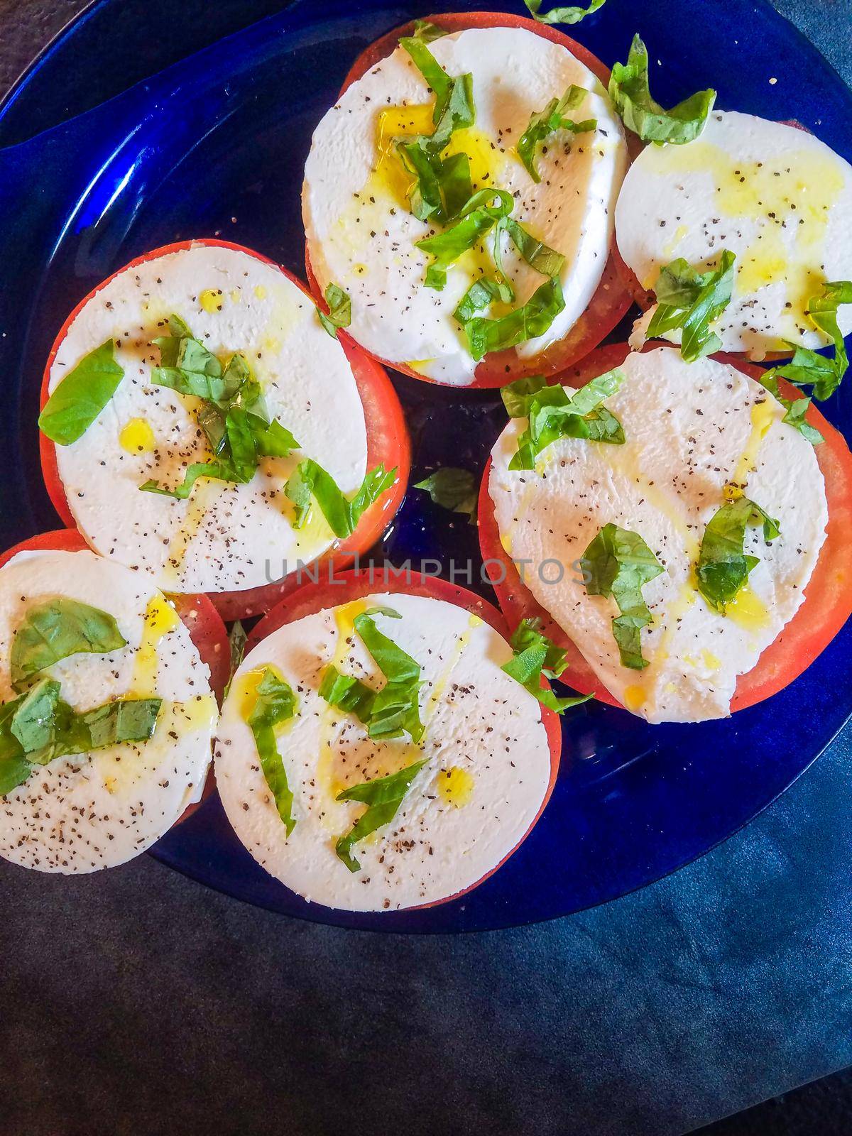 Keto style fresh Italian caprese salad. Mozzarella slices served on slices of beefsteak tomatoes, topped with fresh chopped basil, olive oil, salt and black pepper.