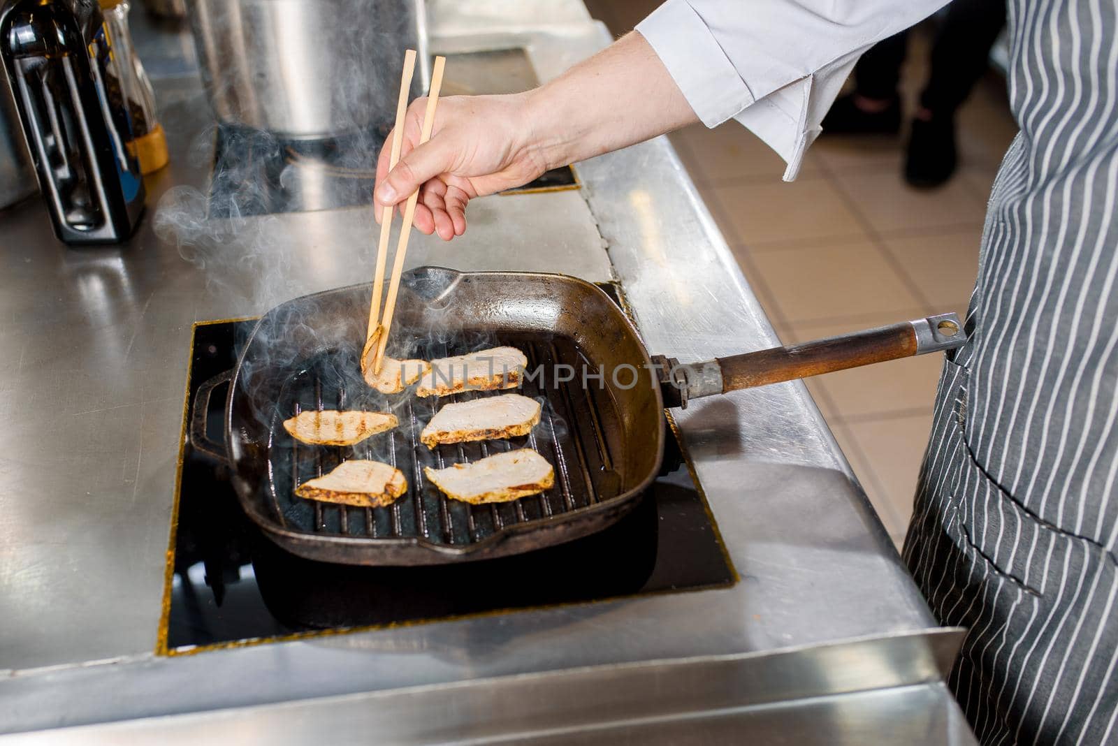 Fried chicken pieces of fillet in a pan. Cooking ramen soup. Chef touches chicken with a japanese sticks for food.