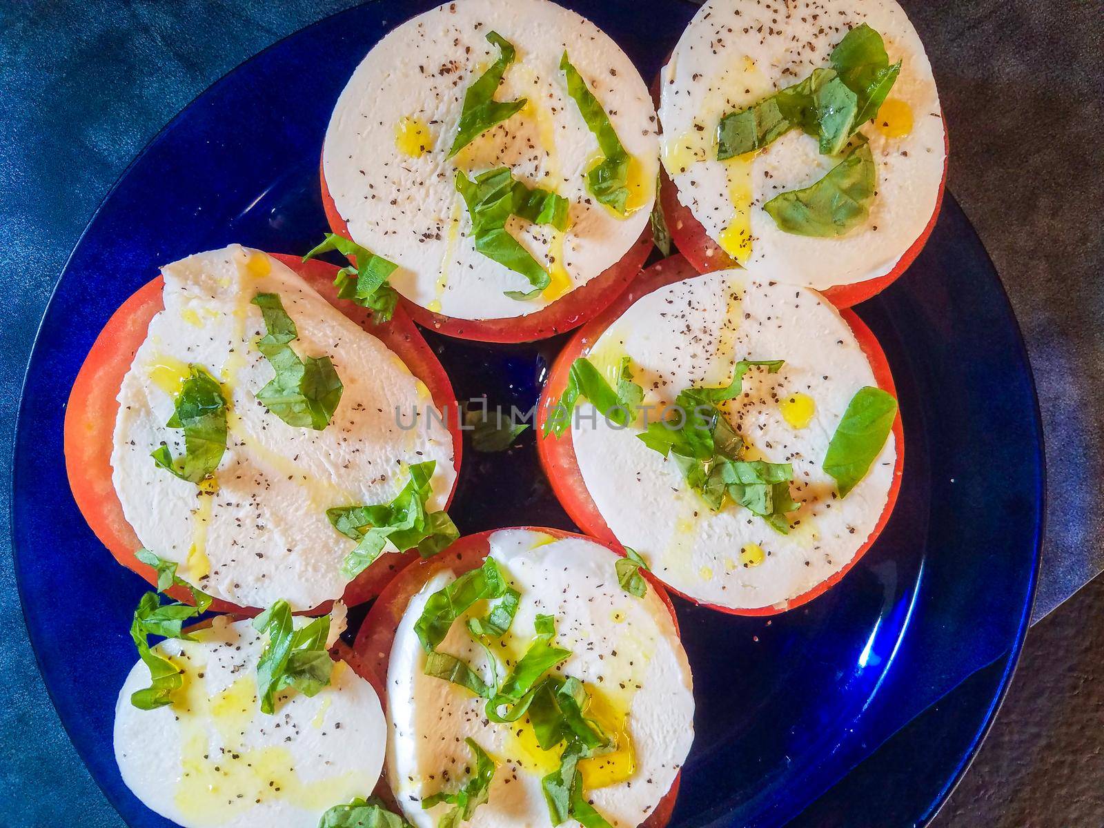 Keto style fresh Italian caprese salad. Mozzarella slices served on slices of beefsteak tomatoes, topped with fresh chopped basil, olive oil, salt and black pepper.