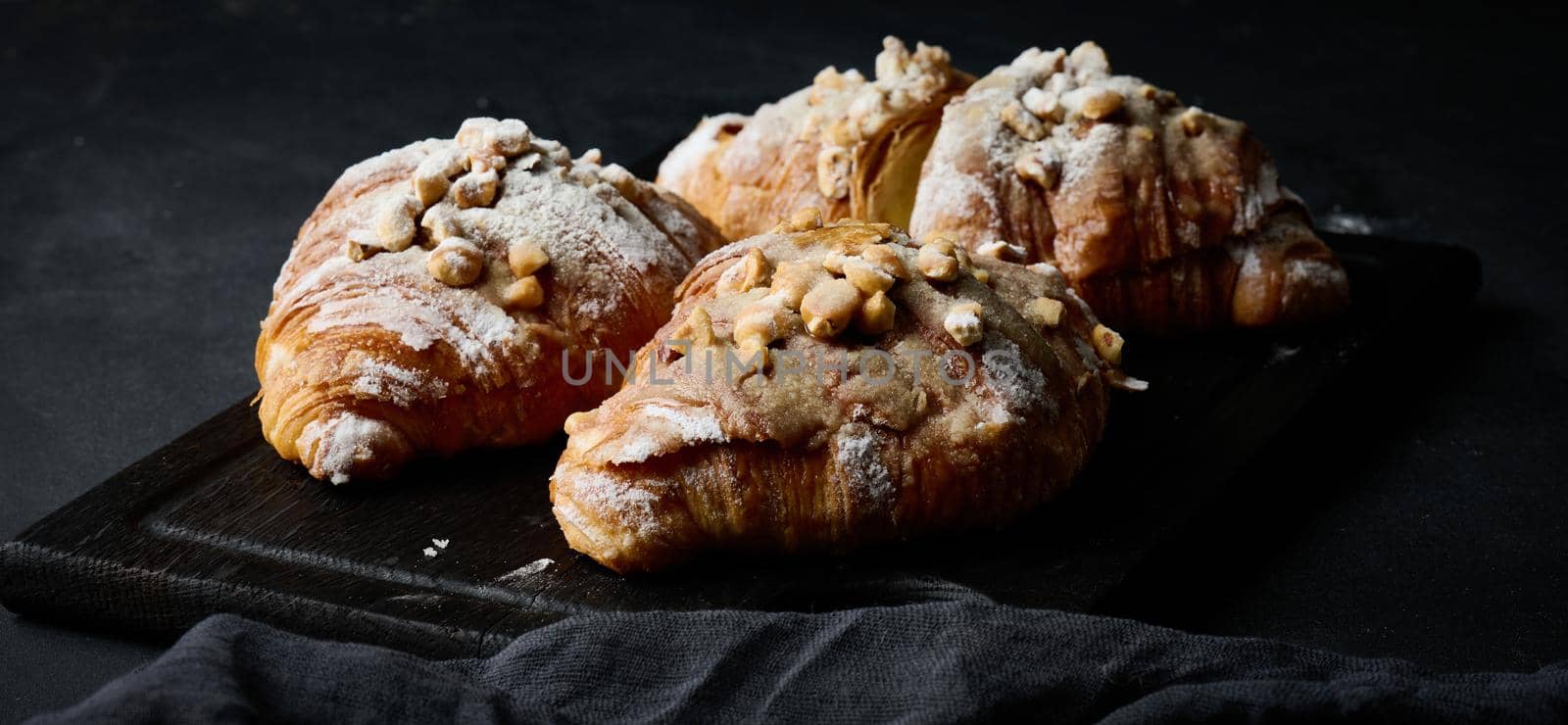 Baked croissants on a black wooden board sprinkled with powdered sugar, close up