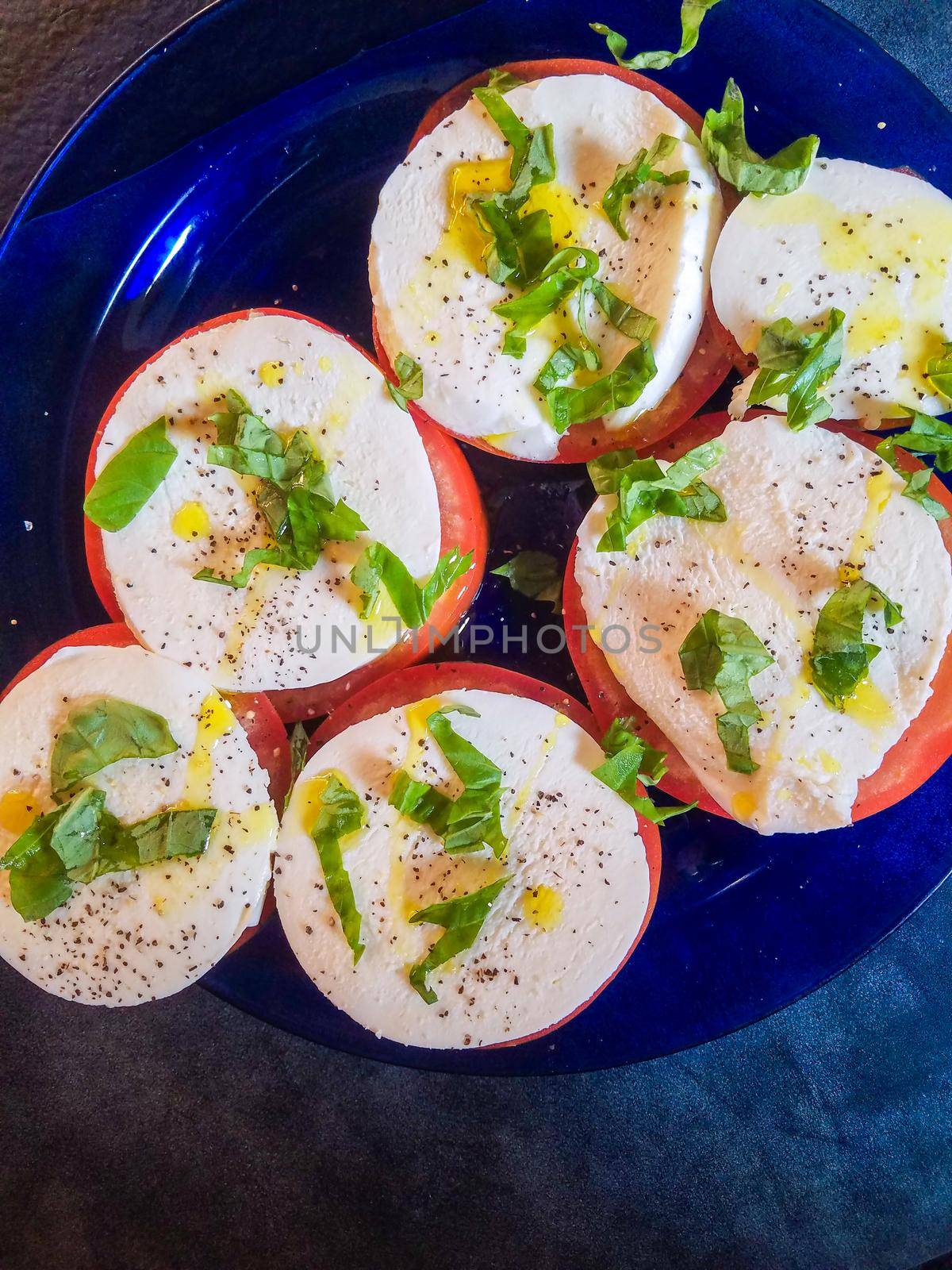 Keto style fresh Italian caprese salad. Mozzarella slices served on slices of beefsteak tomatoes, topped with fresh chopped basil, olive oil, salt and black pepper.