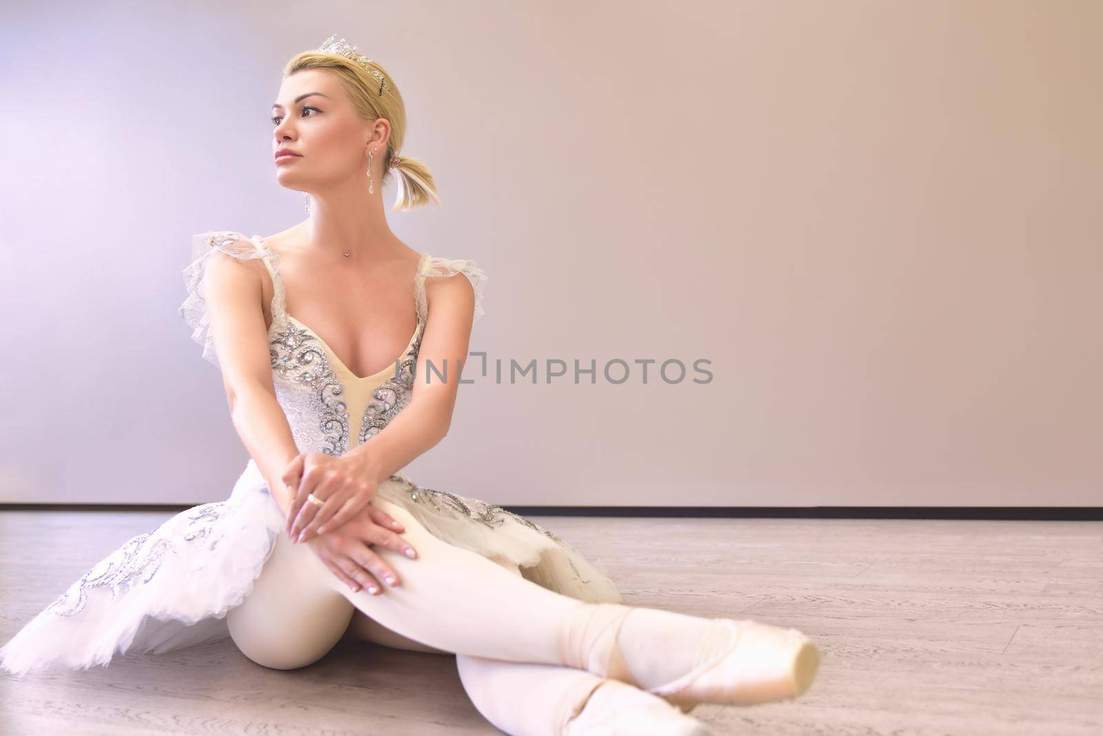 Photo of amazing woman ballerina sitting in a dance studio over beige wall background isolated