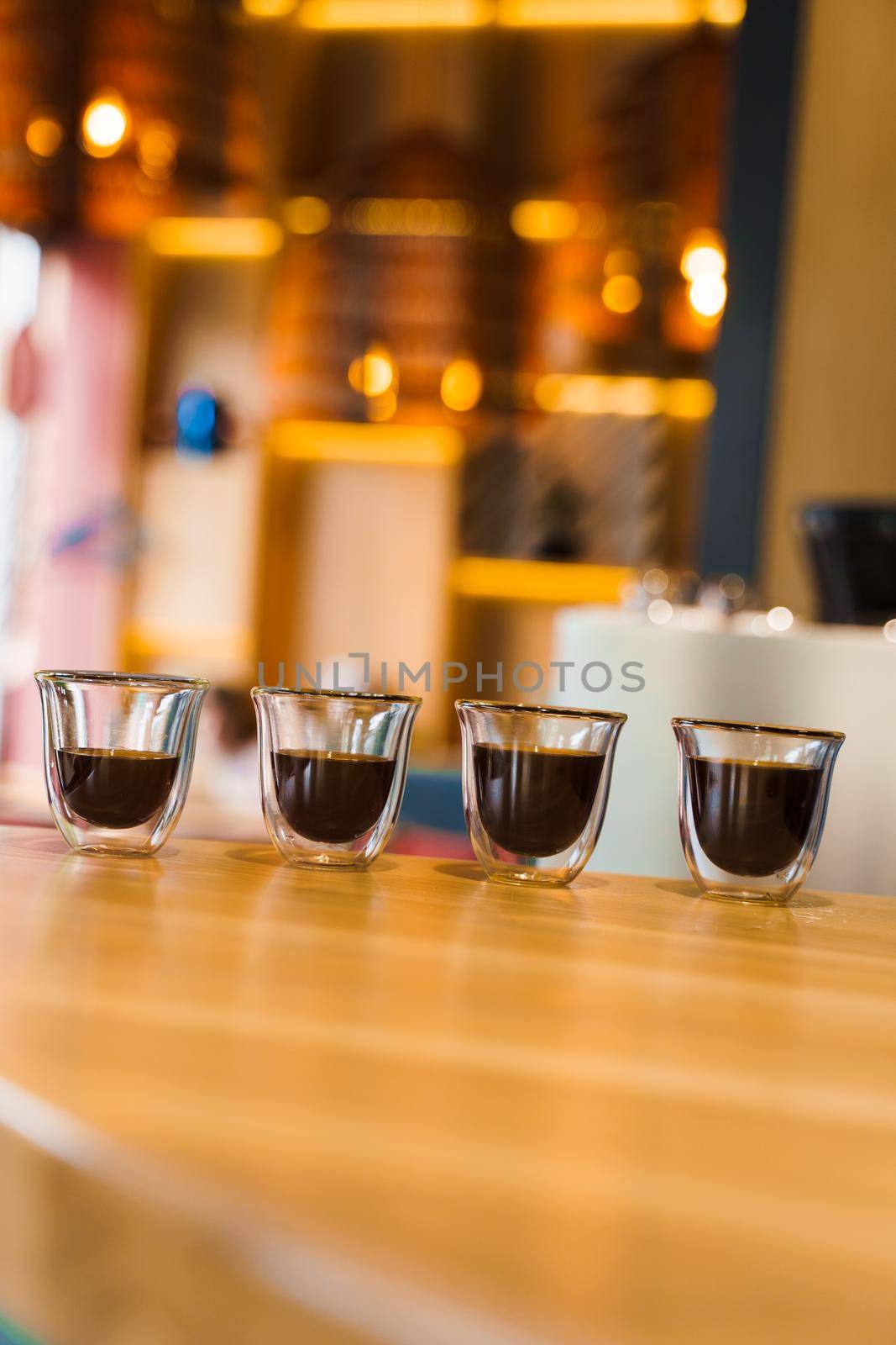 4 Flavored coffee espresso in double glass cup with sun light on background in cafe. Coffee on the wooden table with blurred background by Rabizo