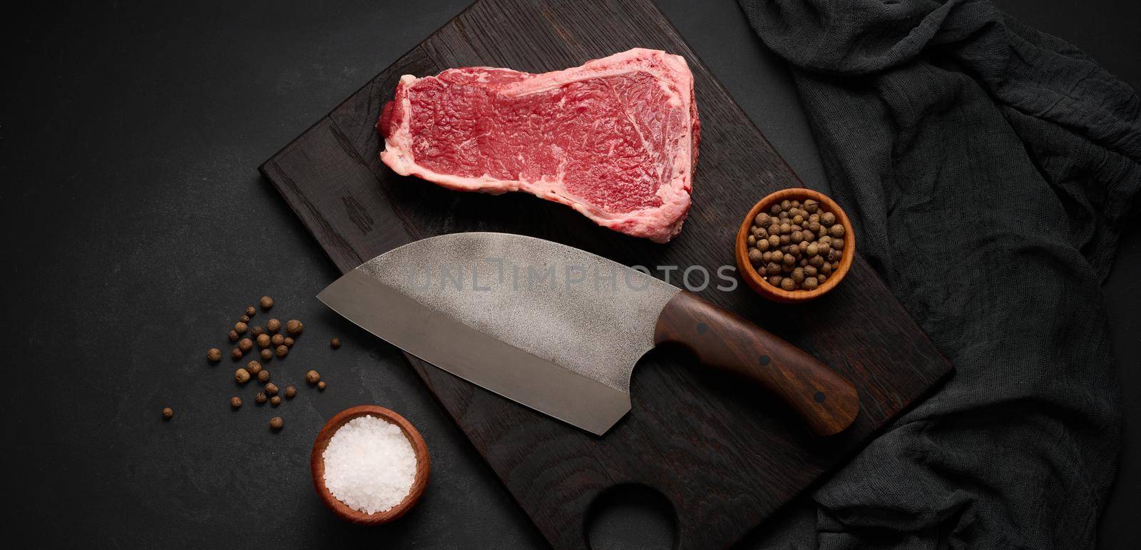 Fresh raw piece of beef meat, striploin steak on a black background, top view. Marbled piece of meat by ndanko