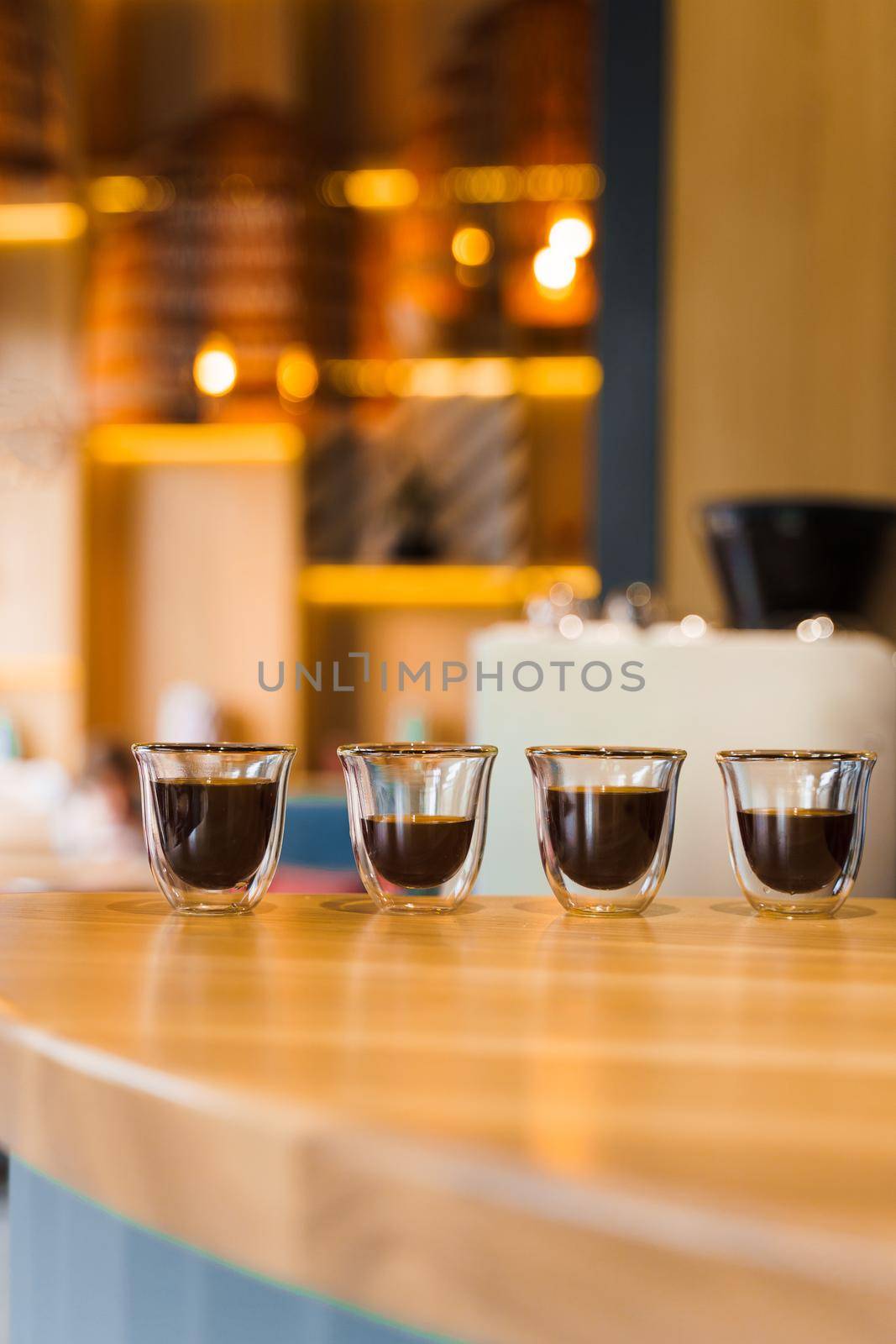 4 Flavored coffee espresso in double glass cup with sun light on background in cafe. Coffee on the wooden table with blurred background.