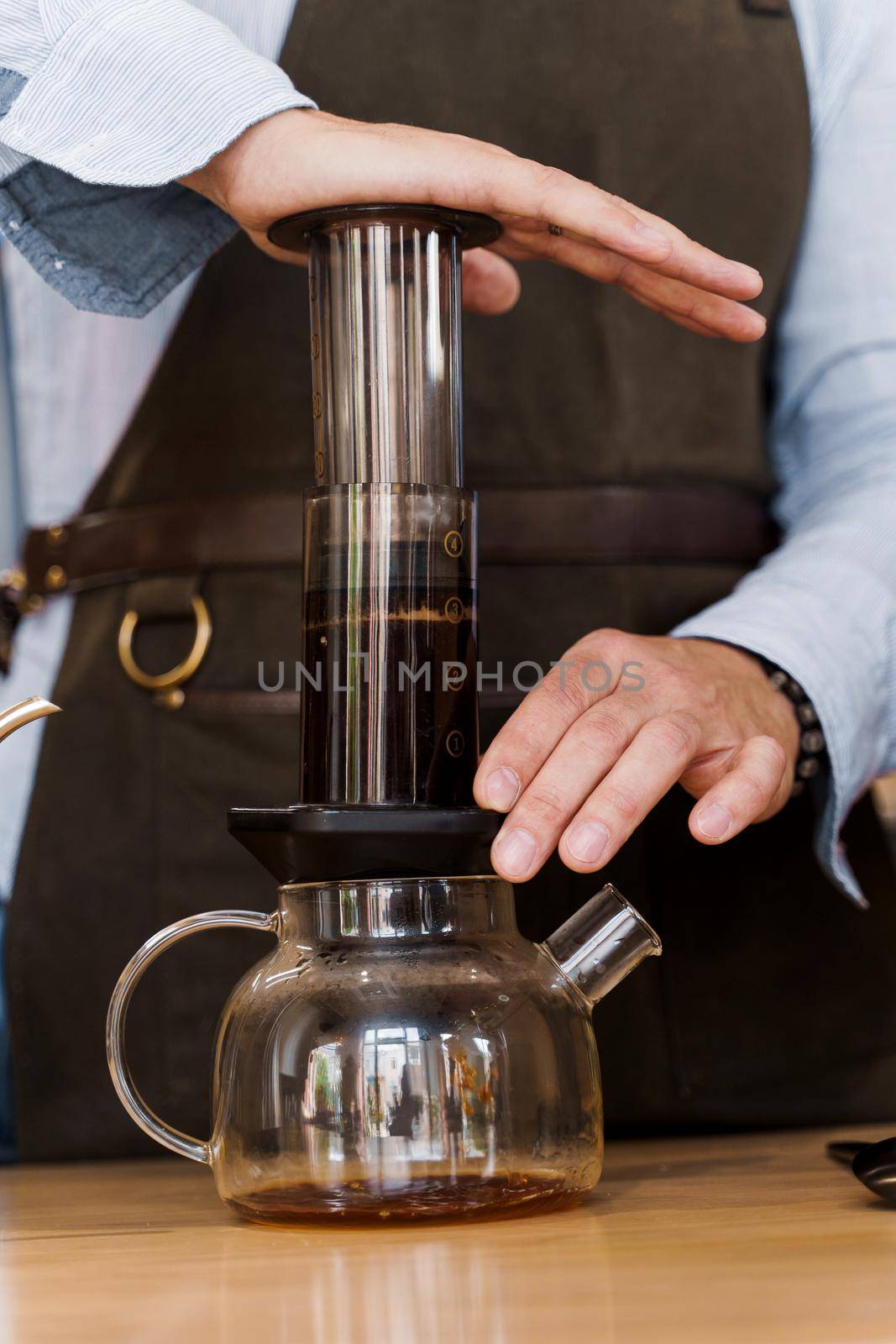 Aeropress coffee close-up: barista press to device and coffee drops pours trought aeropress to pot. Alternative coffee brewing method. Vertical photo