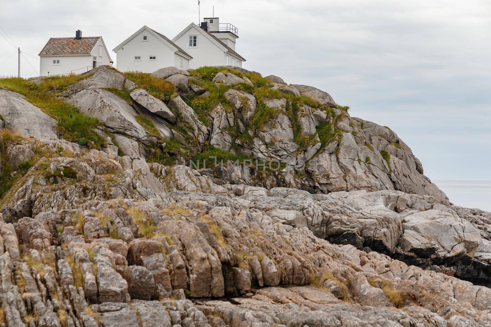 Several white houses stand on the rocky coast of Norway, rocky coast with dramatic sky, the sun breaks through the clouds, sheer cliff. High quality photo