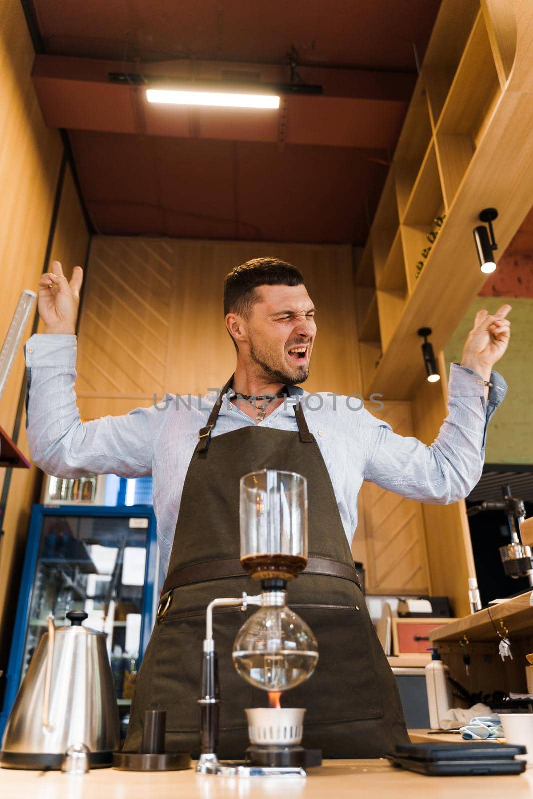 Syphon coffee device with fire heats glass flask in cafe. Emotional barista shows rock and roll. Alternative coffee brewing method