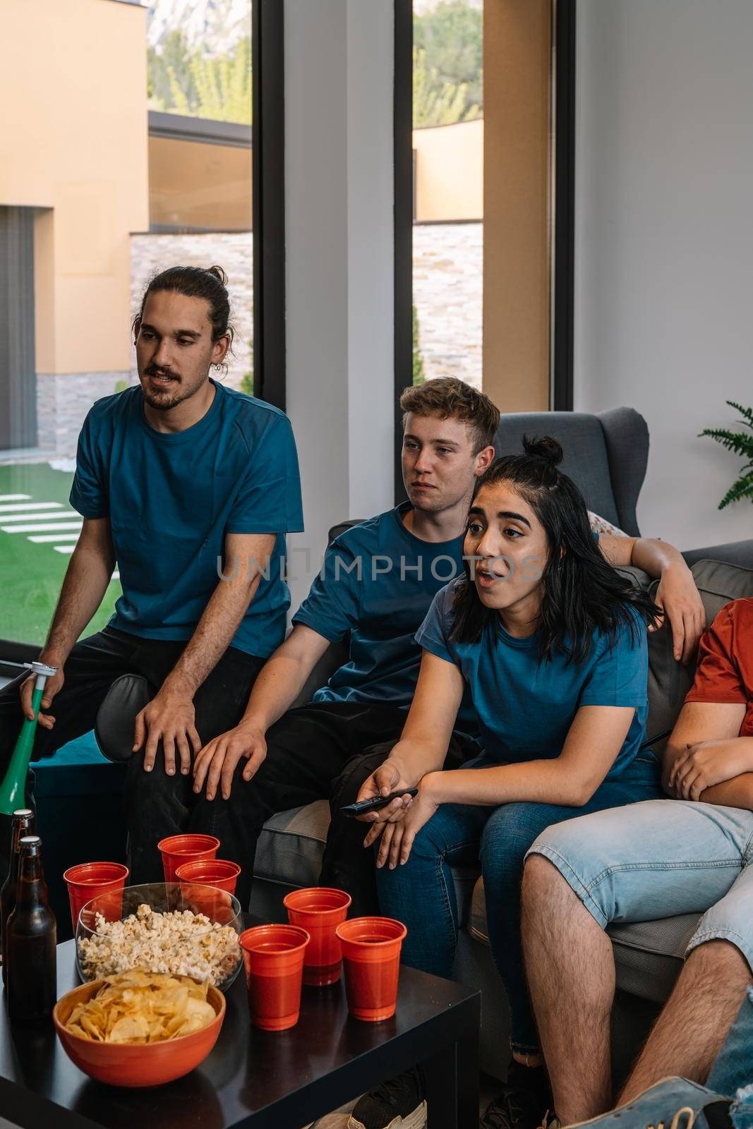 friends enjoying together a sports match broadcast on television. watching a movie. youth eating and drinking. by CatPhotography