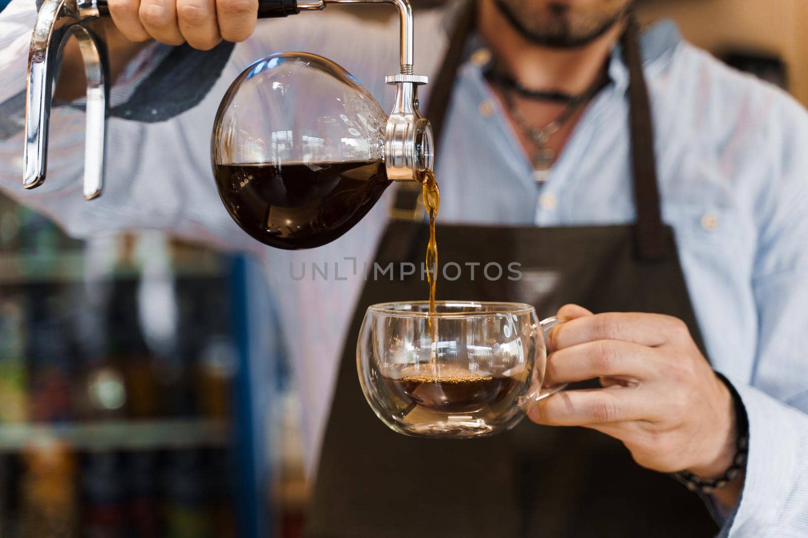 Close-up Syphon alternative method of making coffee. Barista pours hot coffee in syphon device for customers. Coffee brewing in cafe
