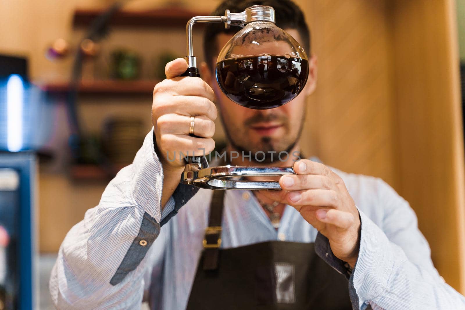 Barista looks at syphon with coffee. Close up alternative cofee making. Coffee brewing using syphon device in cafe.