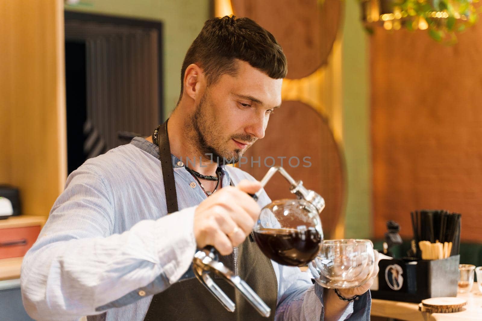 Syphon alternative method of making coffee. Barista pours hot coffee in syphon device for customers. Coffee brewing in cafe