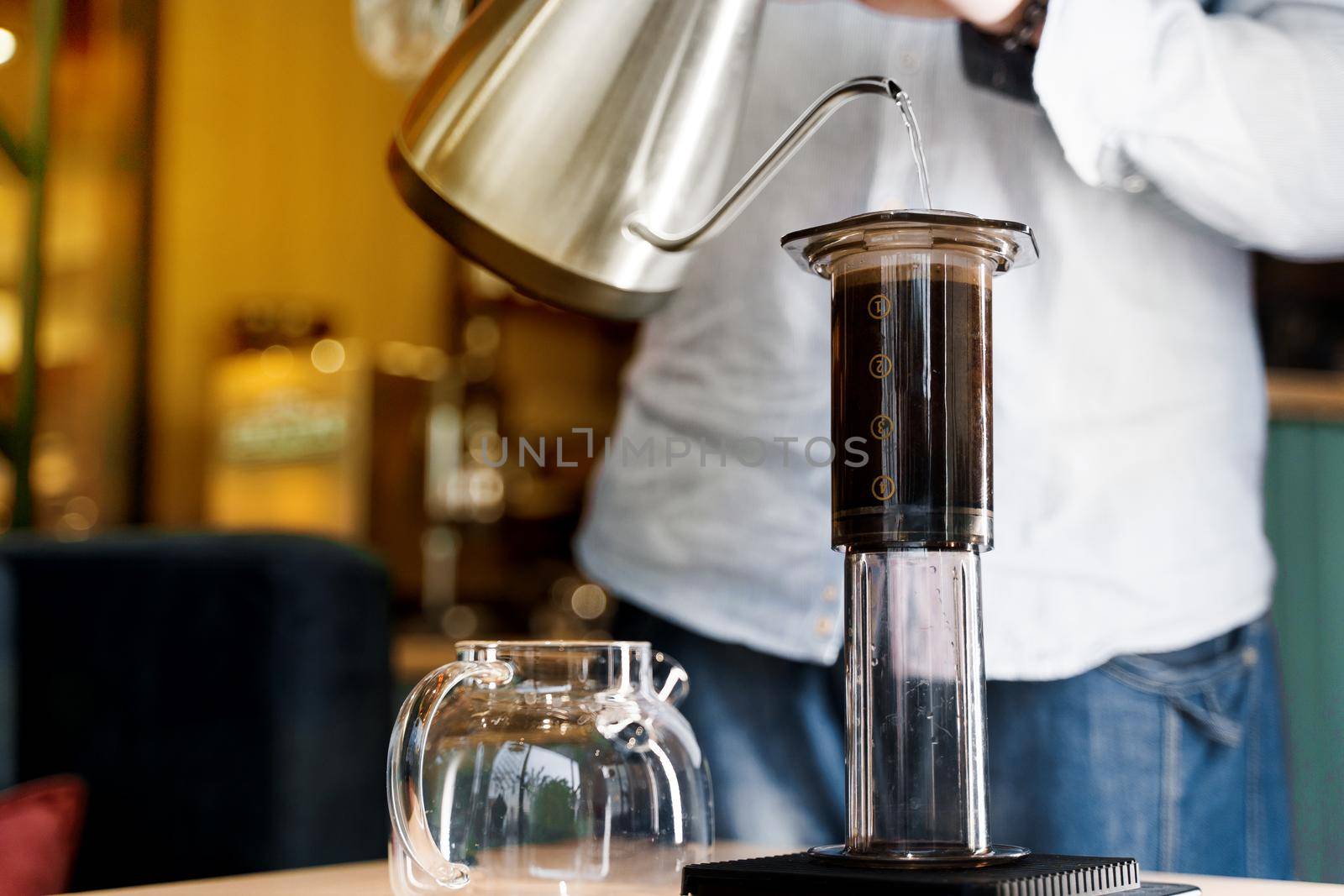 Aeropress coffee close up alternative making by barista in the cafe. Scandinavian coffee brewing method. Barista pours water to aeropress with coffee
