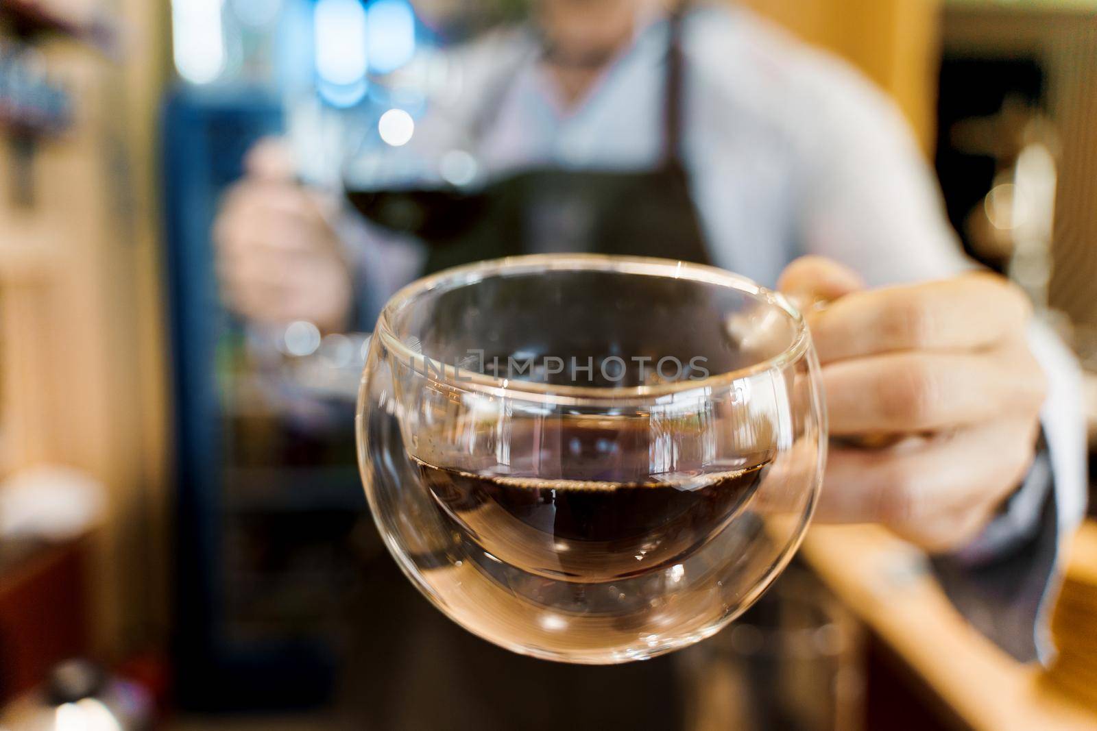 Double glass cup close-up with coffee in cafe. Barista gives a cup of coffee to you. Alternative coffee brewing using Syphon device.