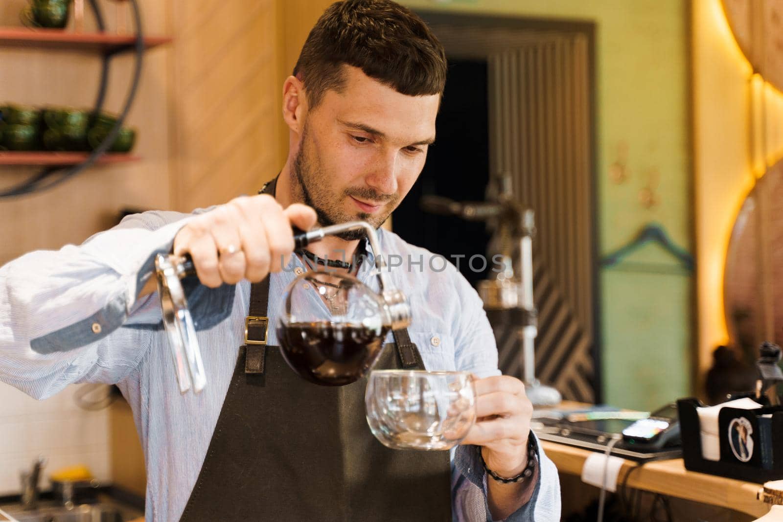 Syphon alternative method of making coffee. Barista pours hot coffee in syphon device for customers. Coffee brewing in cafe