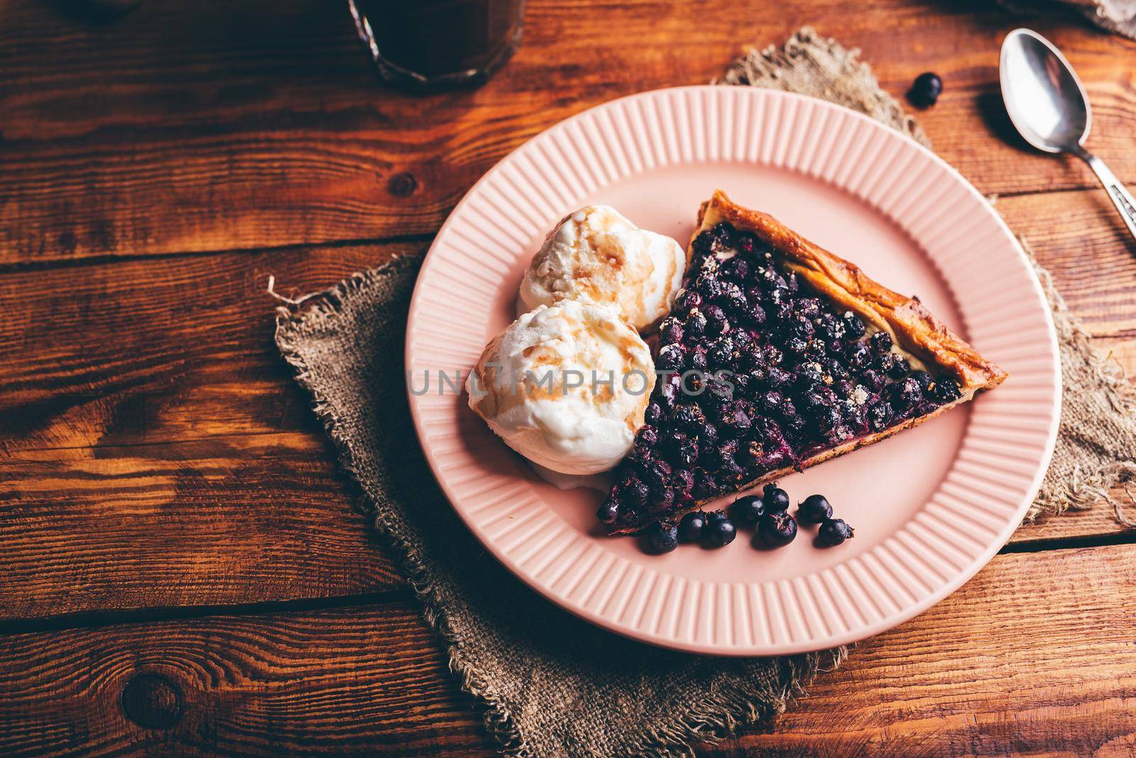 Slice of Homemade Serviceberry Pie and Two Scoops Of Vanilla Ice Cream on Plate over Wooden Table
