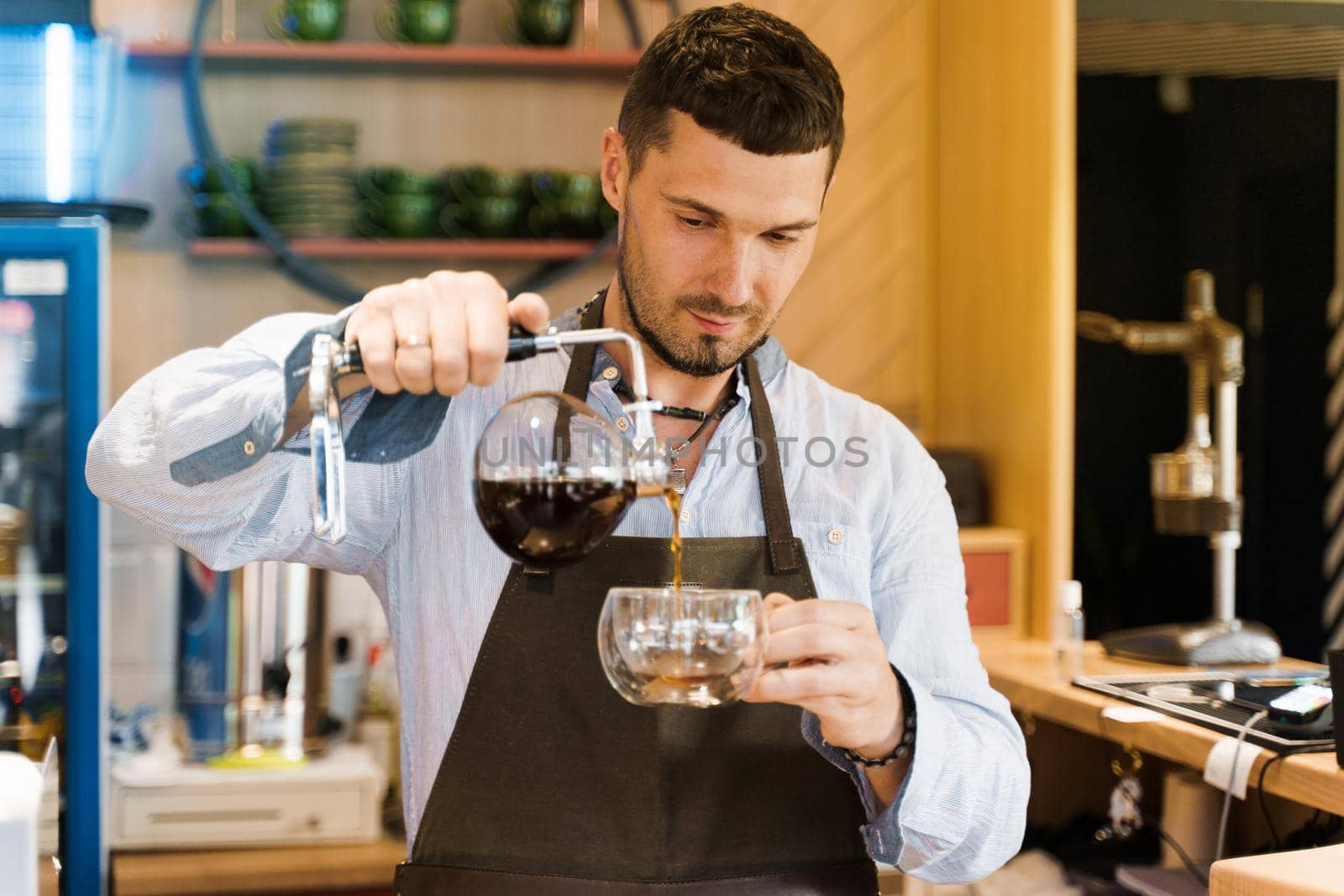 Syphon alternative method of making coffee. Barista pours hot coffee in syphon device for customers. Coffee brewing in cafe