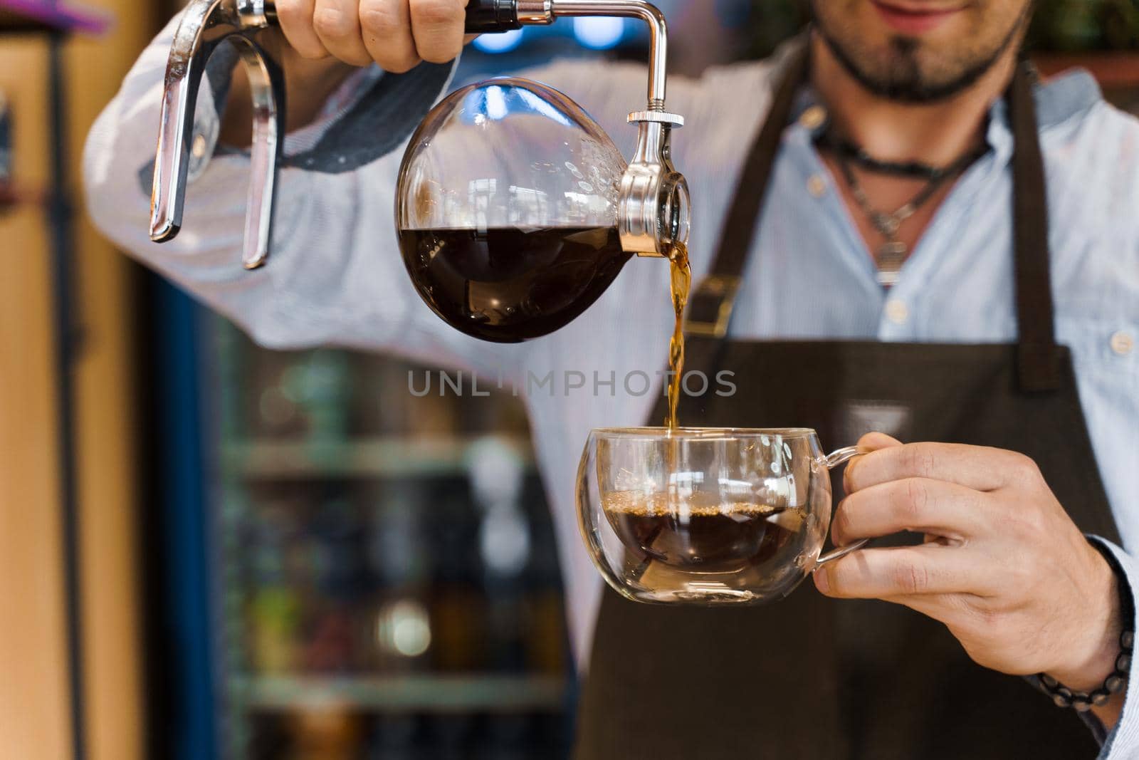 Close-up Syphon alternative method of making coffee. Barista pours hot coffee in syphon device for customers. Coffee brewing in cafe