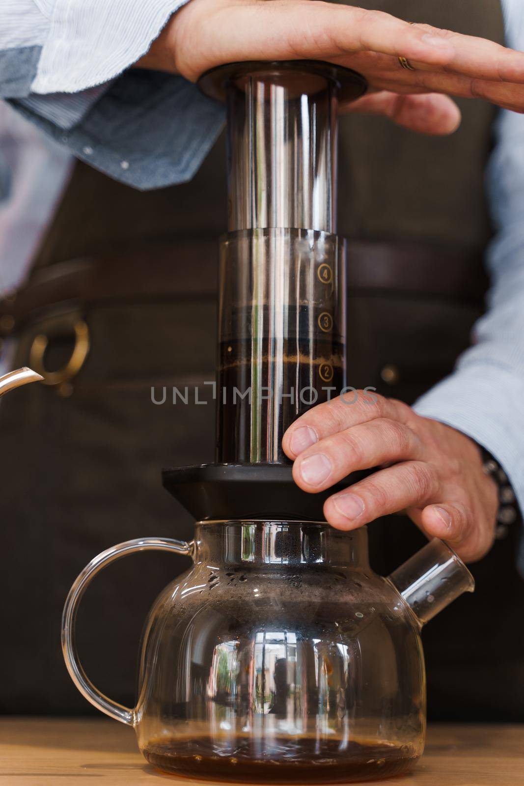 Aeropress coffee close-up: barista press to device and coffee drops pours trought aeropress to pot. Alternative coffee brewing method. Vertical photo