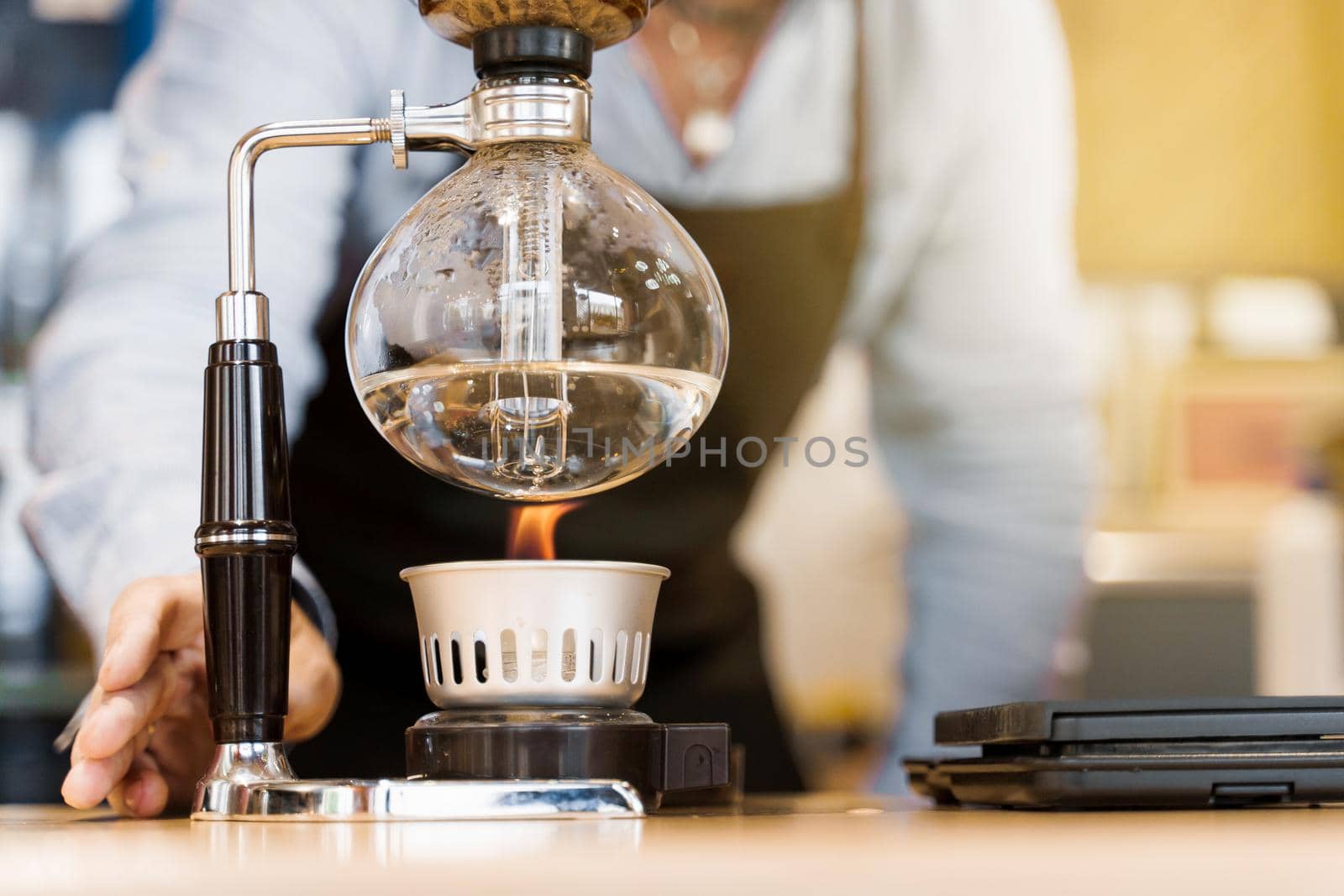Syphon coffee brewing process. Close-up syphon is heating by fire. Barista looking at alternative coffee brewing process on the fire