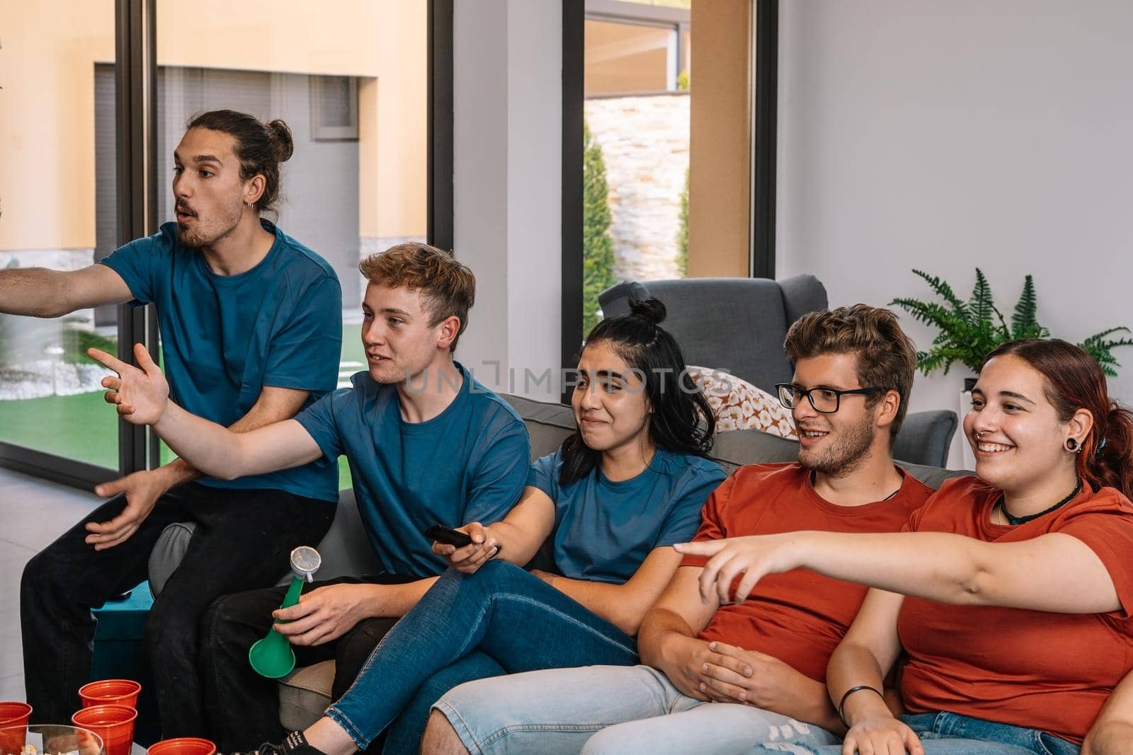 friends enjoying watching sport on television sitting on the sofa. youth watching a movie. changing channels. by CatPhotography