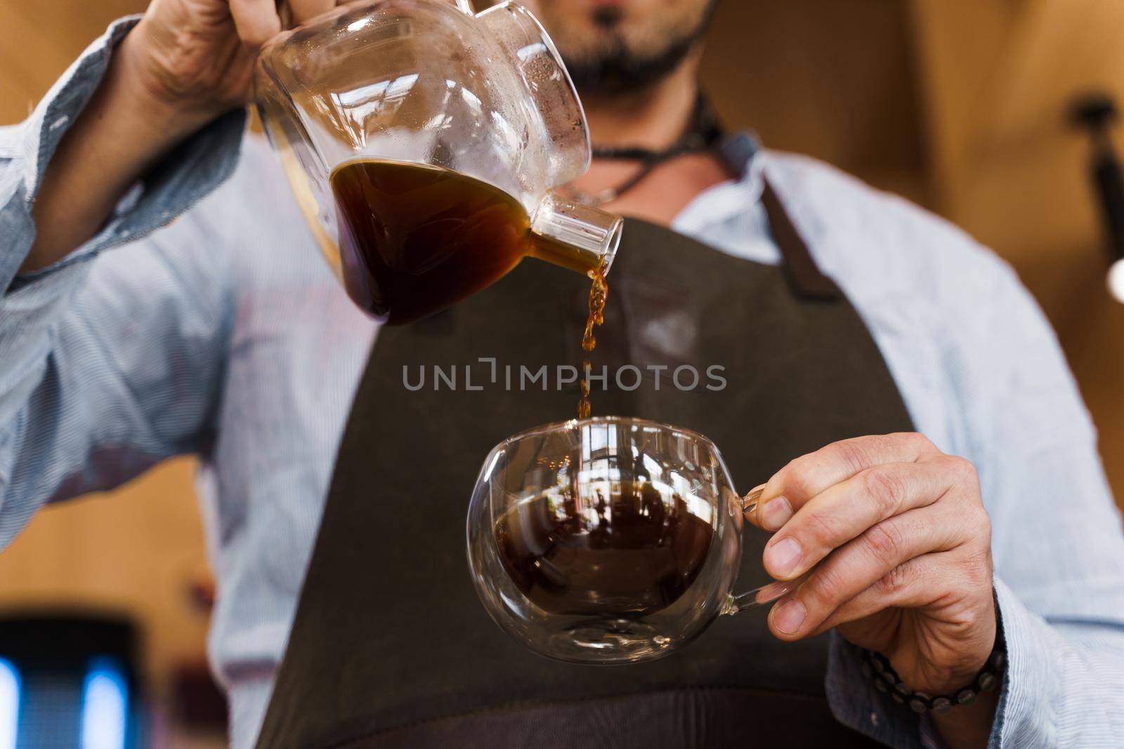 Close-up pouring coffee in double glass cup in cafe by handsome bearded barista. Coffee brewing syphon and aeropress alternative methods