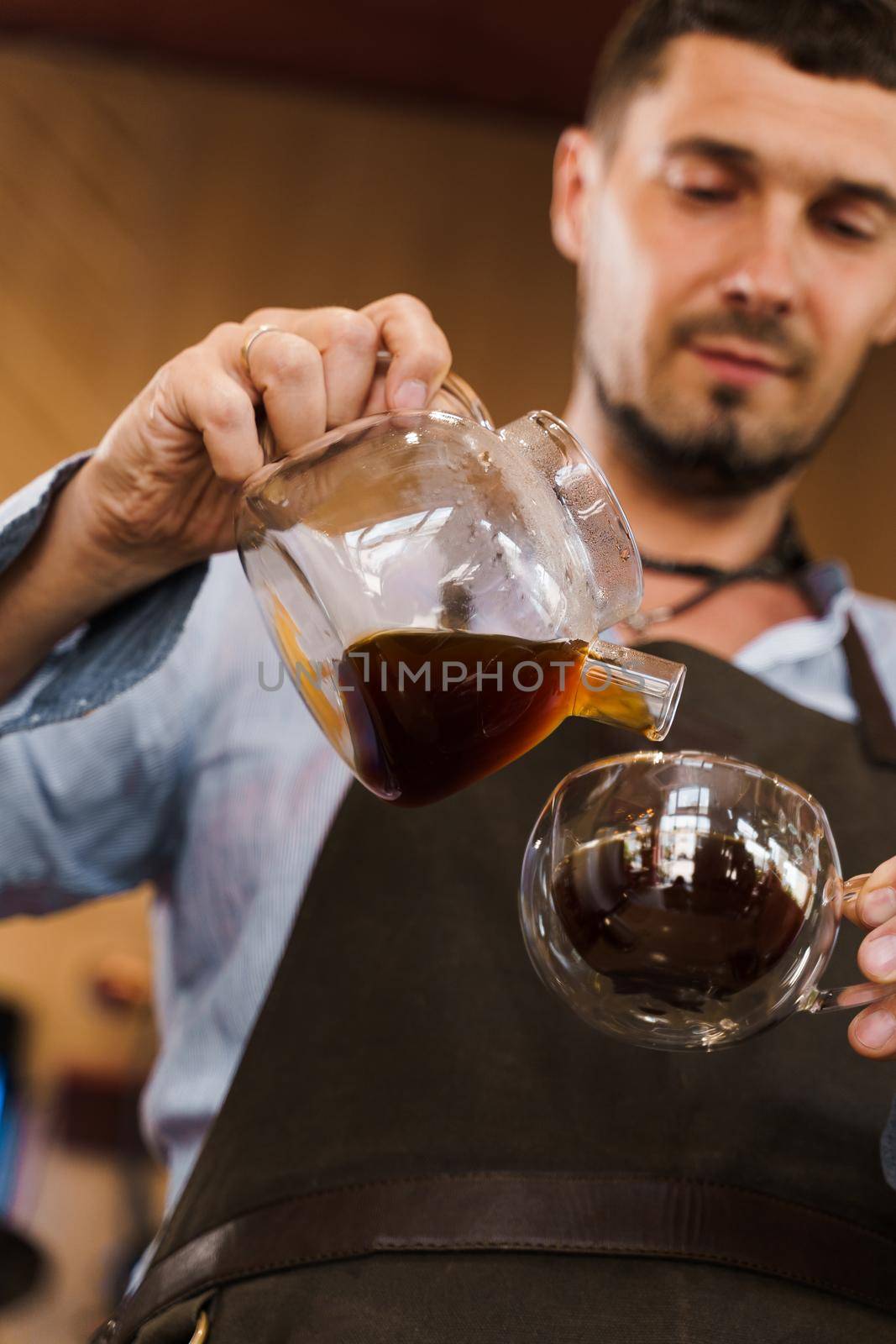 Close-up pouring coffee in double glass cup in cafe by handsome bearded barista. Coffee brewing syphon and aeropress alternative methods