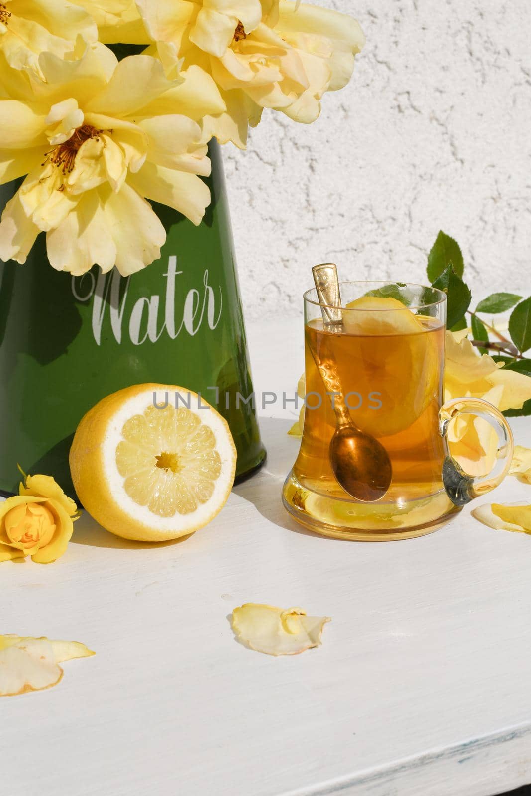 Yellow tea with lemon and a bouquet of yellow roses in a green jug, vintage still life . High quality photo