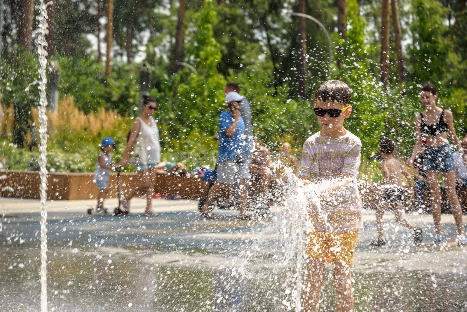 Kyiv, Ukraine - August 01, 2021: Boys jumping in water fountains. Children playing with a city fountain on hot summer day. Happy friends having fun in fountain. Summer weather. Friendship, lifestyle and vacation.