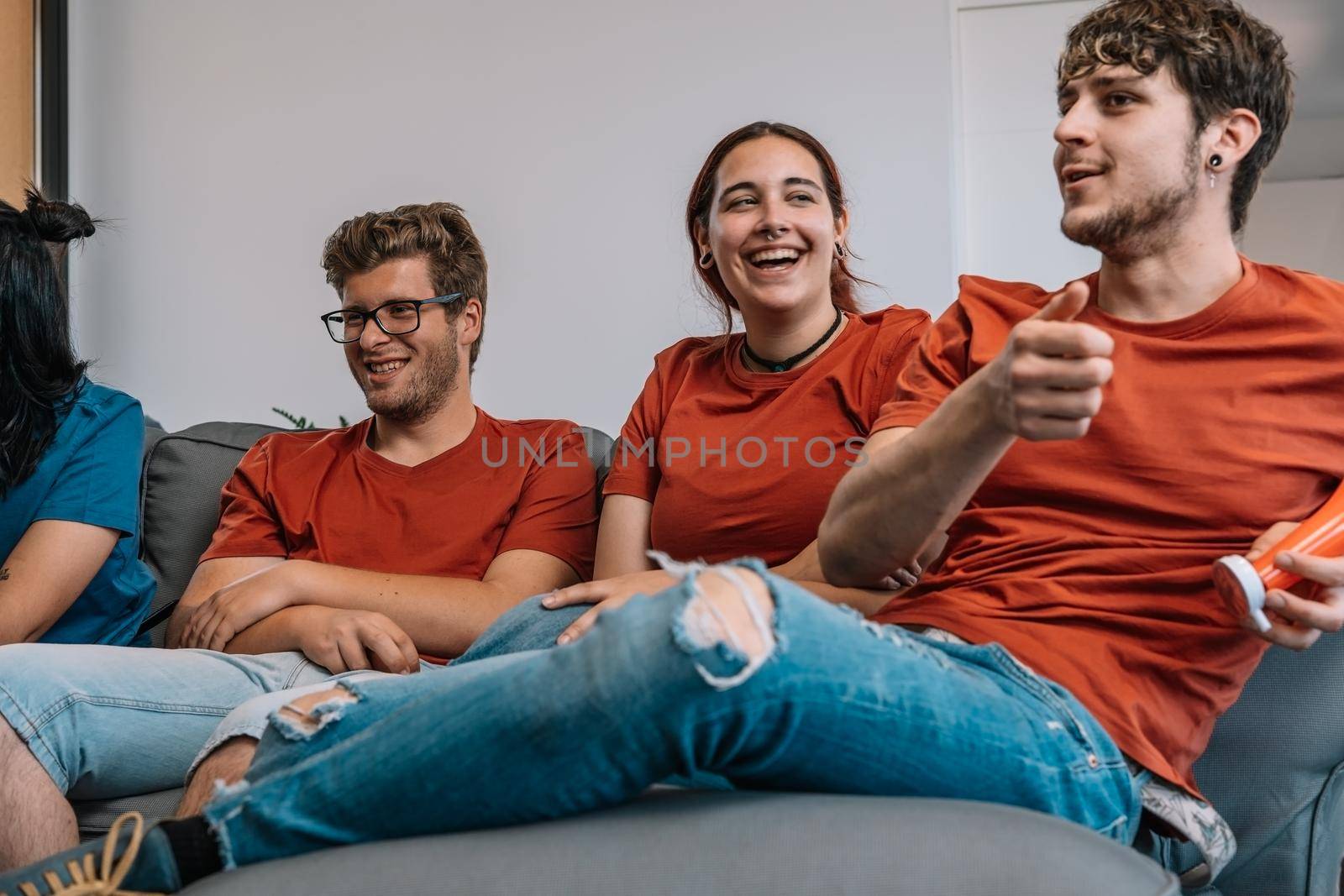 friends sitting on the sofa watching TV and laughing. watching a film. watching sport on TV. sitting on the sofa in the living room, natural light.