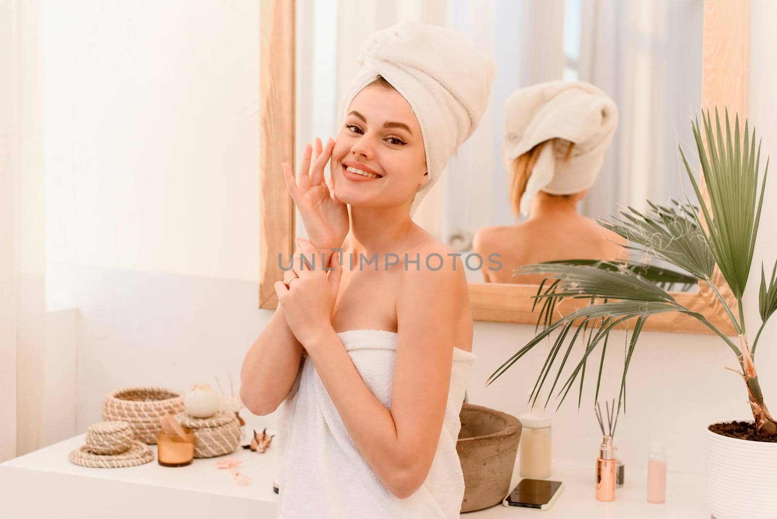 A young woman comes out of the shower wrapped in a towel, smiling and looking at the camera. Spa treatments at home, skin care