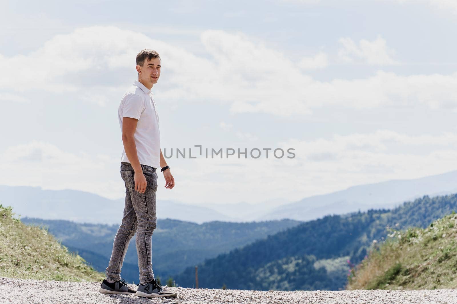 Handsome man is walking on the green hills background. Advert for travel agency. Tourism. Travelling in the mountains.