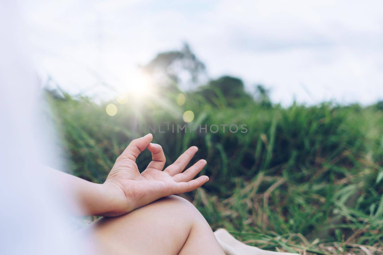 Woman practicing yoga lesson, breathing, meditating exercise, outdoor in grass field. Well being, wellness concept