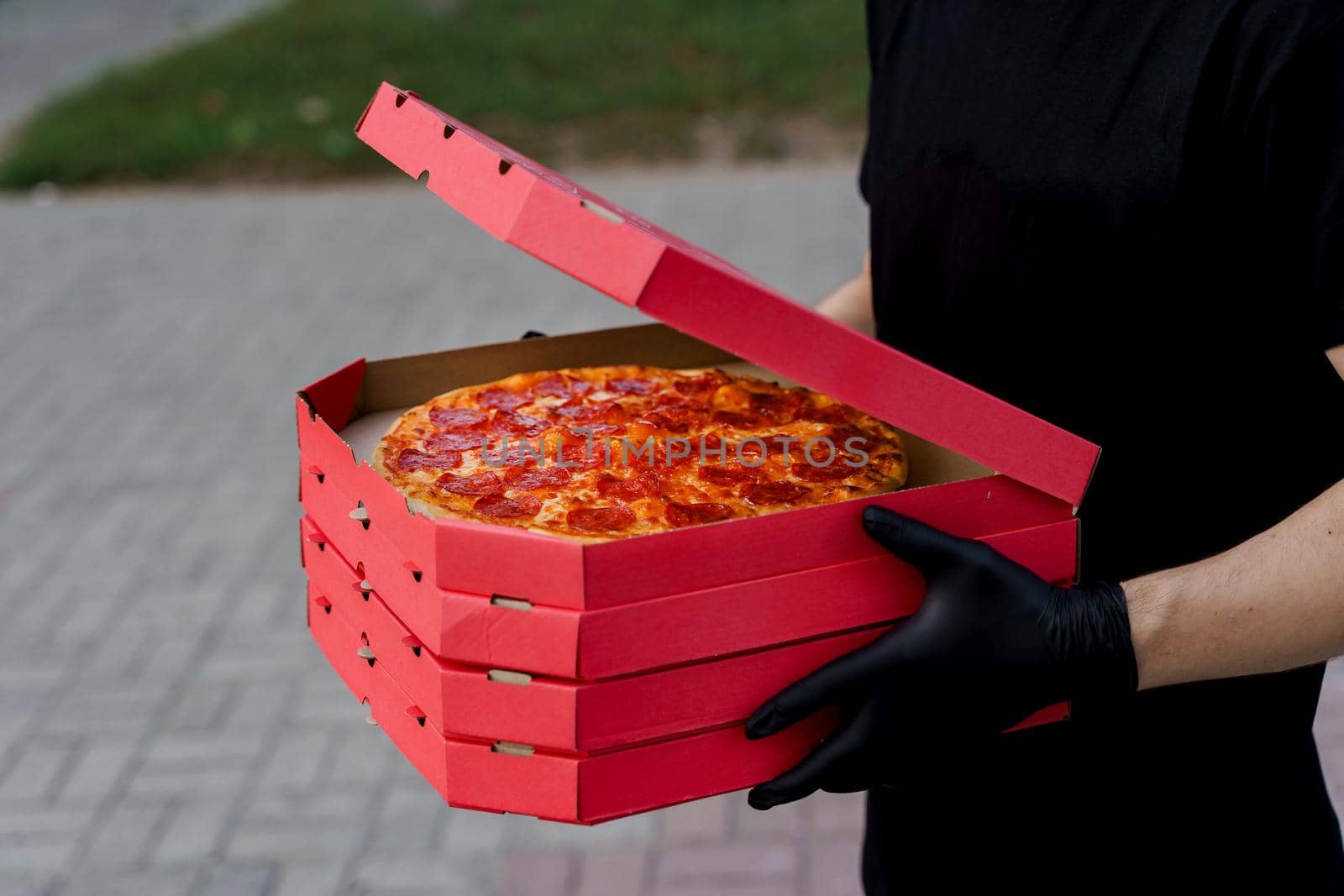Safety pizza delivery from restaurant. Food courier in black medical gloves. Isolated photo of pizza with cheese and salami. Stop pandemic coronavirus covid 19 by Rabizo