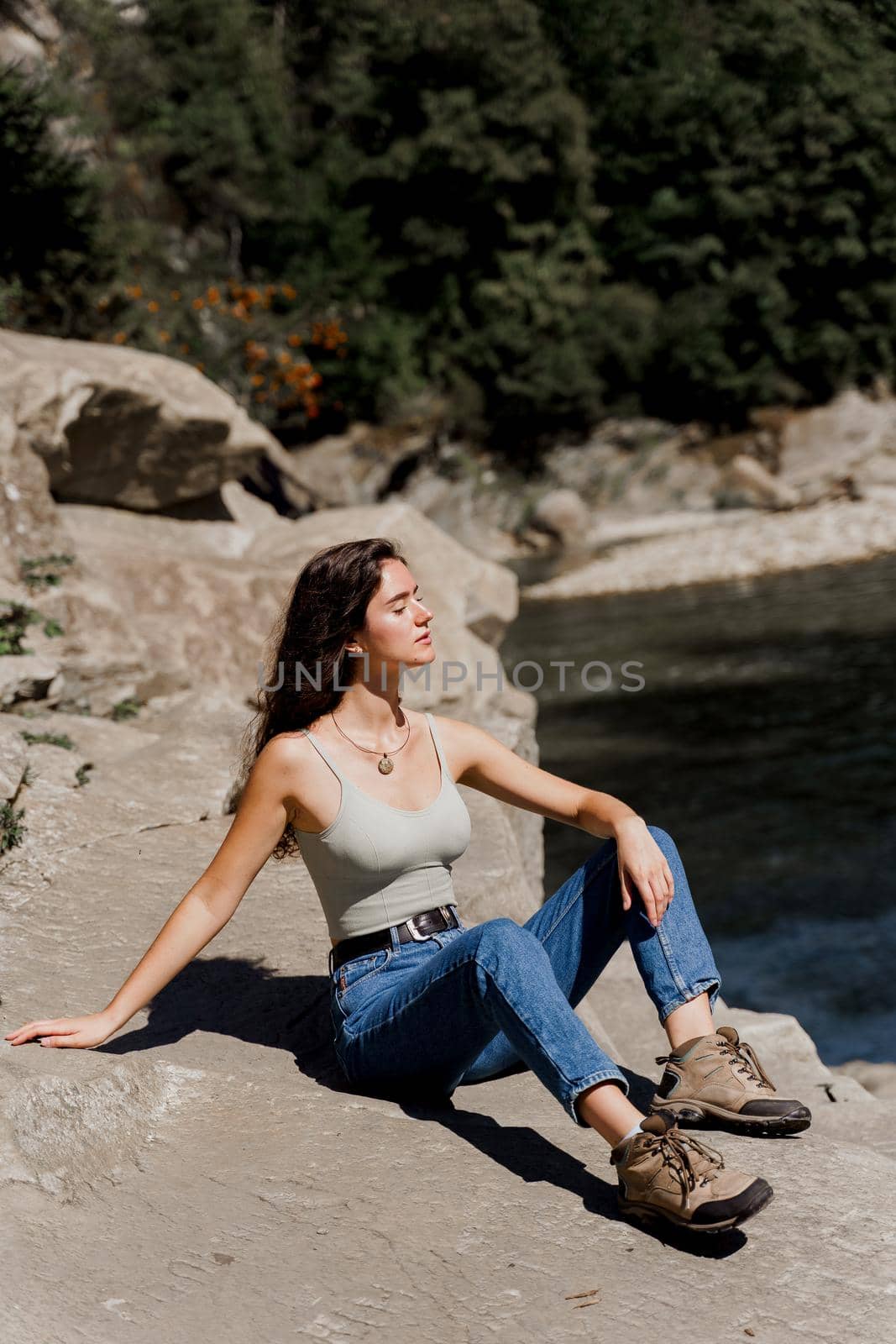 Traveler girl is sitting on the rock near waterfall and looking toward. Travelling in Karpathian mountains. Cascade waterfall. Beautiful landscape