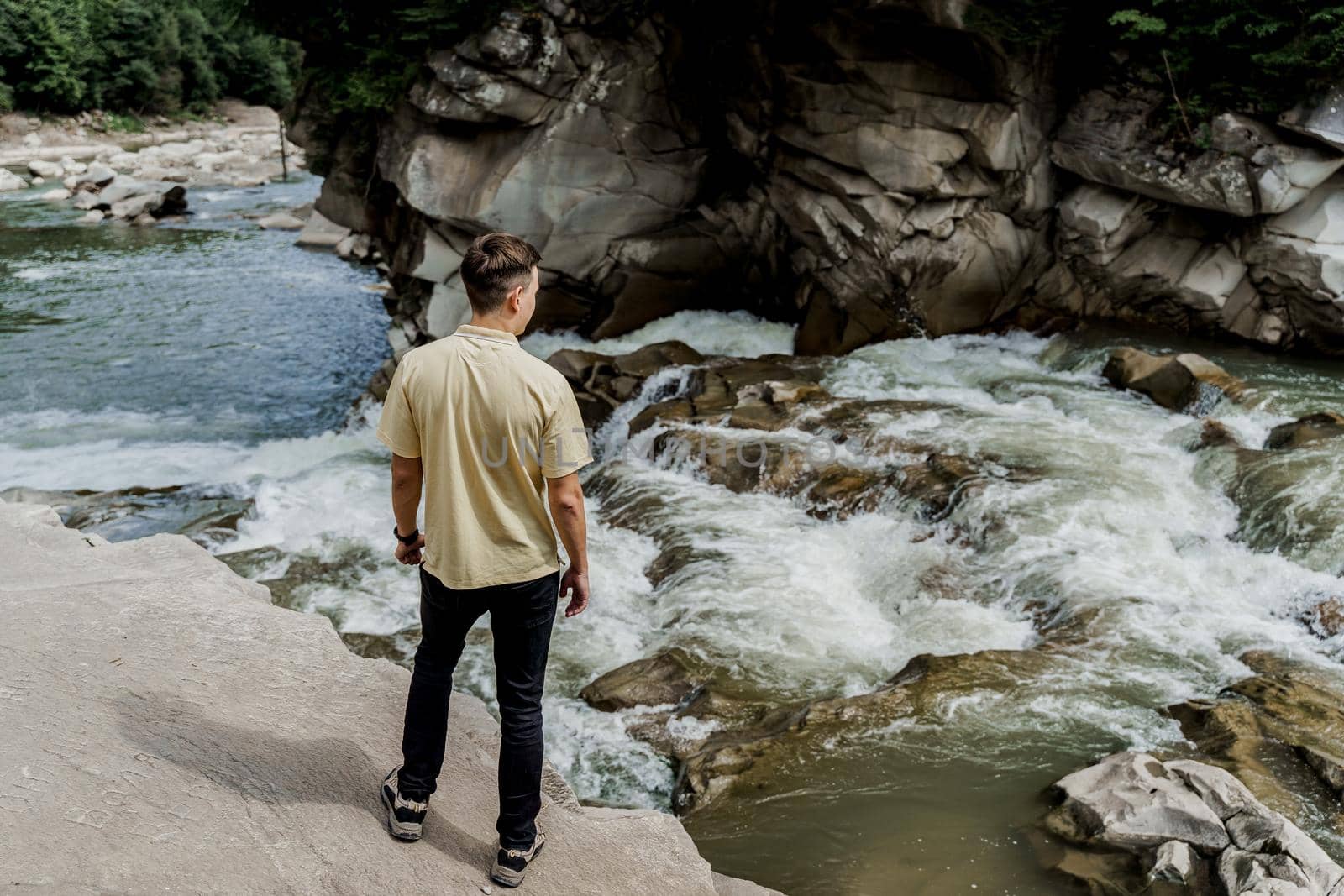 Traveler man on the rock near waterfall. Travelling in Karpathian mountains. Cascade waterfall. Beautiful landscape