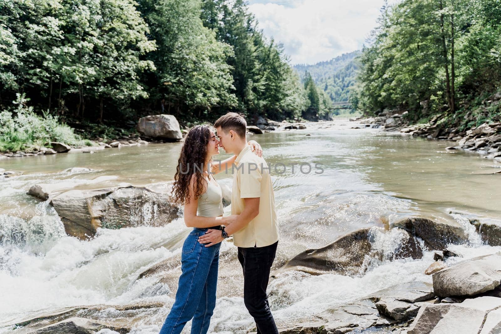 Love story of couple. Travelling in Karpathian mountains. Waterfall in mountain river. Cascade waterfall and happy couple hugging each other
