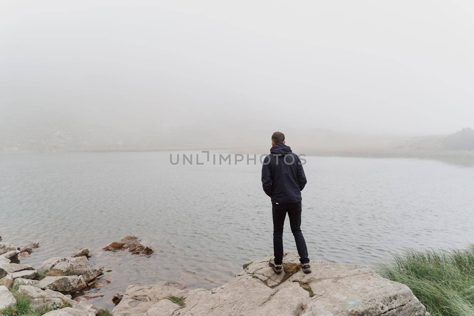 Man tourist is travelling and standing on the rocks near foggy lake. Hiking and climbing up to the top of the mountain. Tourism in Ukraine.